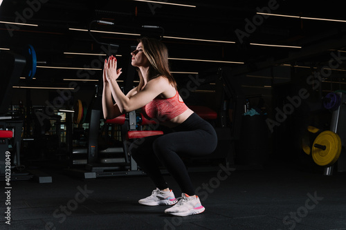 Young beautiful woman is doing squats with her own weight in the gym.