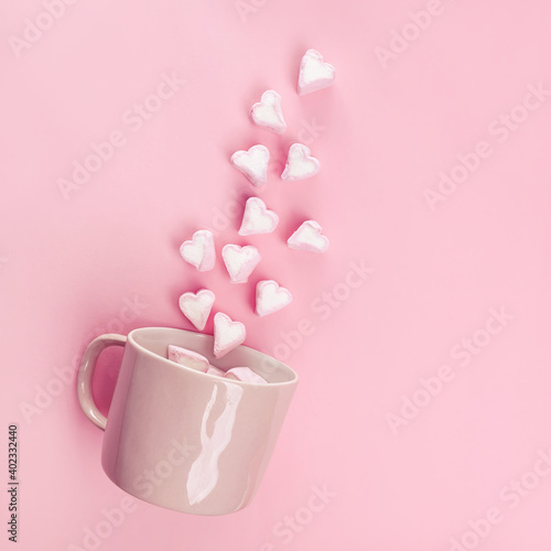 Marshmallows in the shape of hearts flying out of pink cup.