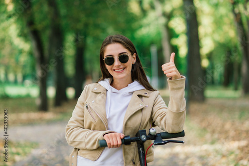 Young woman riding an electric scooter in an autumn park. Green transport, traffic jam problems.