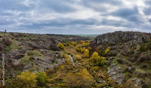 A picturesque stream flows in the Aktovsky Canyon, surrounded by autumn trees and large stone boulders
