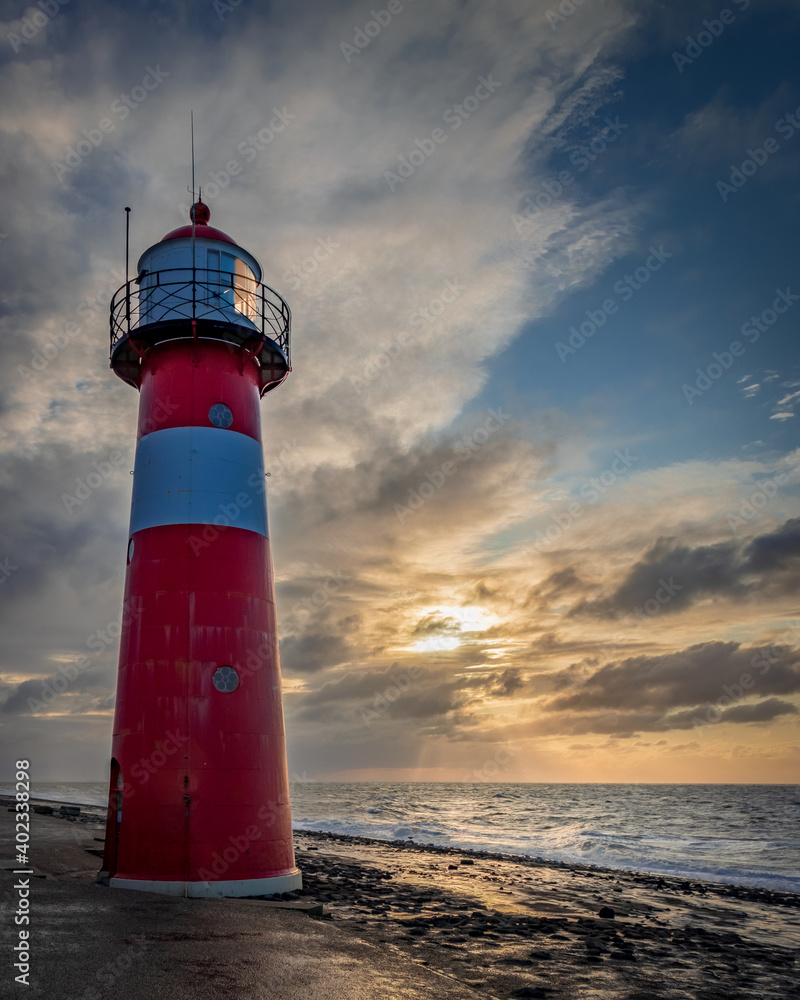 Tuinposter met Red and white striped lighthouse in front of clouded sunset sky at the shore of Westkappelle in the Netherlands #402338298
