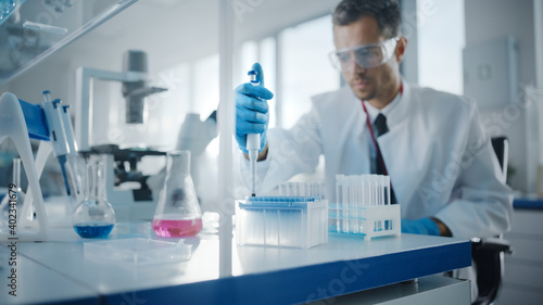 Medical Development Laboratory: Male Scientist Uses Micro Pipette for Filling Test Tubes with Liquid, Conducting Experiment. Big Pharmaceutical Lab with Specialists Research Medicine, Biotechnology