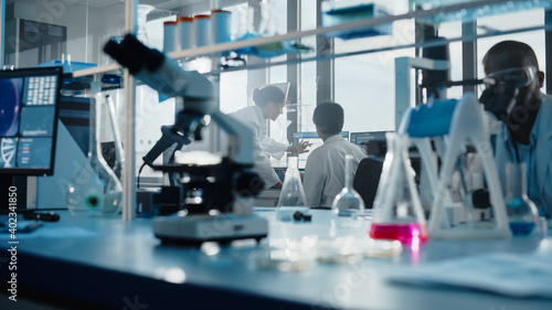 Medical Science Laboratory with Diverse Multi-Ethnic Team of Biotechnology Scientists Developing Drugs, Microbiologist Working on Computer with Display Showing Gene Editing Interface.