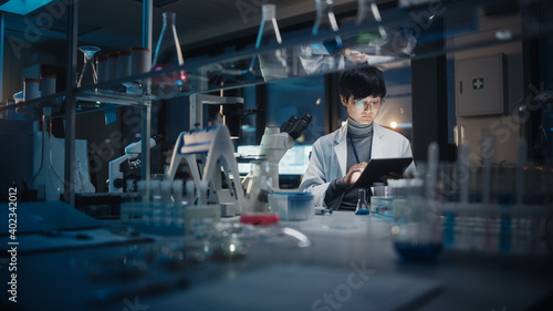 Photos Medical Development Laboratory: East Asian Scientist Uses Digital Tablet Computer, Microscope, Conducting Experiment
