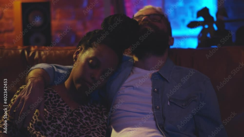 Portrait of diverse relaxed couple embracing and sleeping together on a couch in front of tv Portrait of diverse relaxed couple embracing and sleeping together on a couch in front of tv