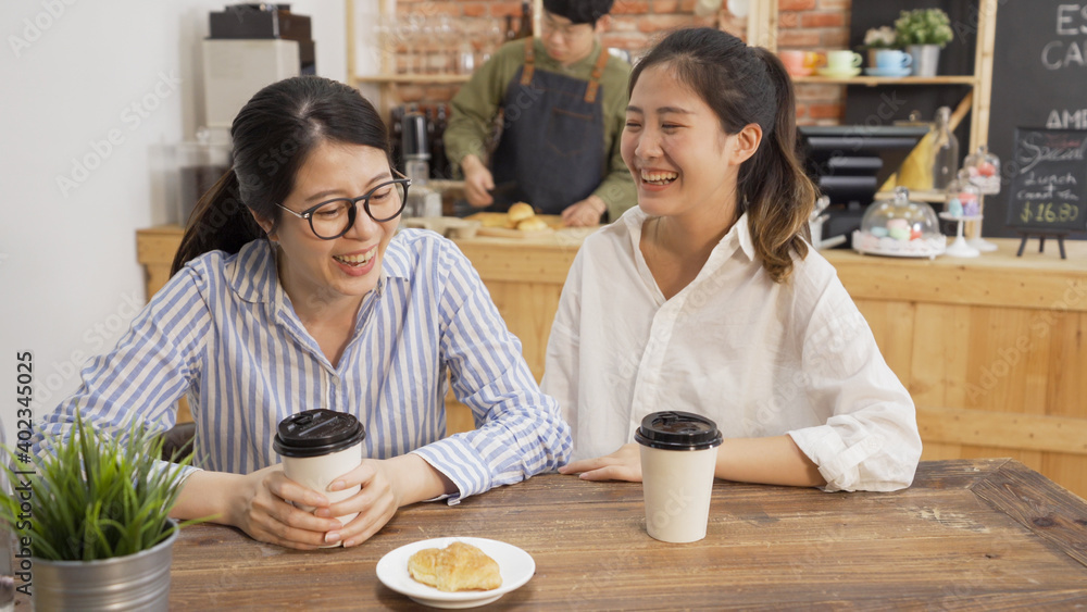 Two asian female coworkers talking at coffee shop while waiting for meal. girls colleagues friends chatting and laughing enjoy lunch break time together in cafe. man waiter prepare customer order Two asian female coworkers talking at coffee shop while waiting for meal. girls colleagues friends chatting and laughing enjoy lunch break time together in cafe. man waiter prepare customer order