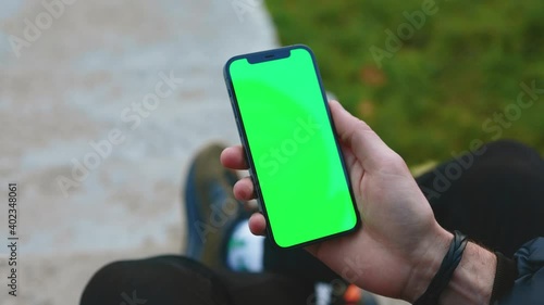 Shot of man hands use phone with vertical green screen outdoors. Sitting. Touchscreen finger internet cellphone scrolling. Close up. Slow motion