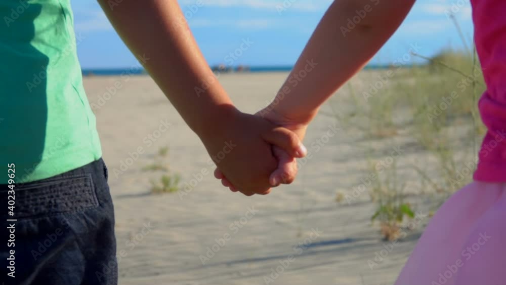 Close-up of little boy and girl in pink skirt holding hands on the beach on a sunny day Close-up of little boy and girl in pink skirt holding hands on the beach on a sunny day