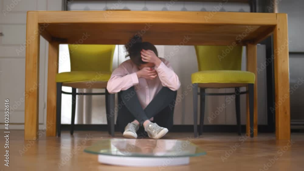 Young stressed woman obsessed with diet sitting under table at home with scales on foreground