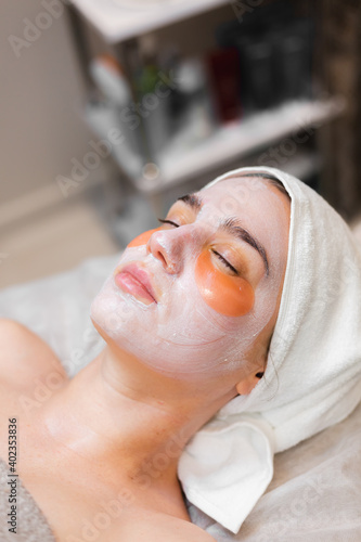 A young girl in a beauty salon in a cosmetology room lies on a bed relaxes with a mask on her face and patches under her eyes