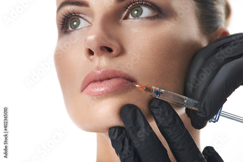Young beautiful woman receiving injection of filler in lips. Injection cosmetology. Closeup on white background. Lips augmentation and correction concept