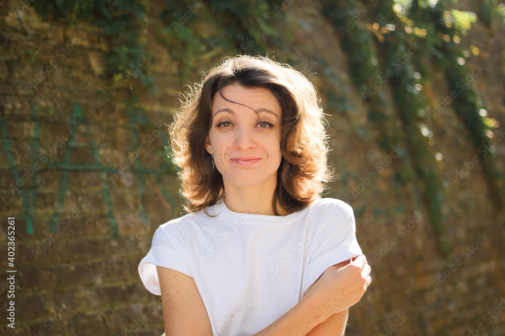 Female portrait of beautiful student, pretty girl with short hair in white t-shirt spending time outdoors near old stone wall during sunny spring or summer day Female portrait of beautiful student, pretty girl with short hair in white t-shirt spending time outdoors near old stone wall during sunny spring or summer day