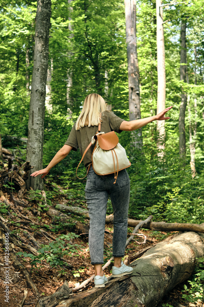 A woman traveler walks through the forest. Beautiful nature landscape in woods. Hiking journey on tourist trail. Outdoor adventure. Travel and exploration. Healthy lifestyle, leisure activities A woman traveler walks through the forest. Beautiful nature landscape in woods. Hiking journey on tourist trail. Outdoor adventure. Travel and exploration. Healthy lifestyle, leisure activities