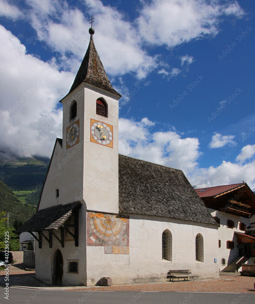 Street with the small gothic village church of St Jakob and its traditional wood shingle roof in Rabland, Vinschgau region, South Tyrol in Italy