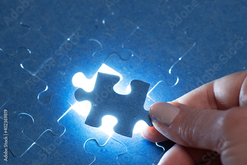 The missing piece of the puzzle with light, the concept of completing a big job, the final of the project, the successful solution of business problems. The hand puts the last piece of the jigsaw