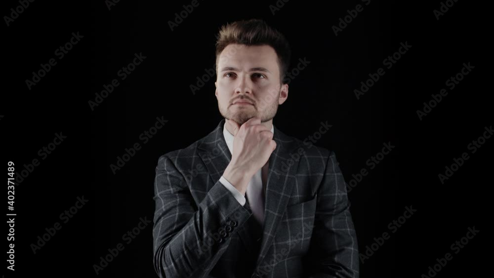 Handsome businessman wearing suit thinks about work and touches his beard with hand isolated on black background. Portrait of young bearded man wear plaid blazer business suit, serious thoughtful look Handsome businessman wearing suit thinks about work and touches his beard with hand isolated on black background. Portrait of young bearded man wear plaid blazer business suit, serious thoughtful look