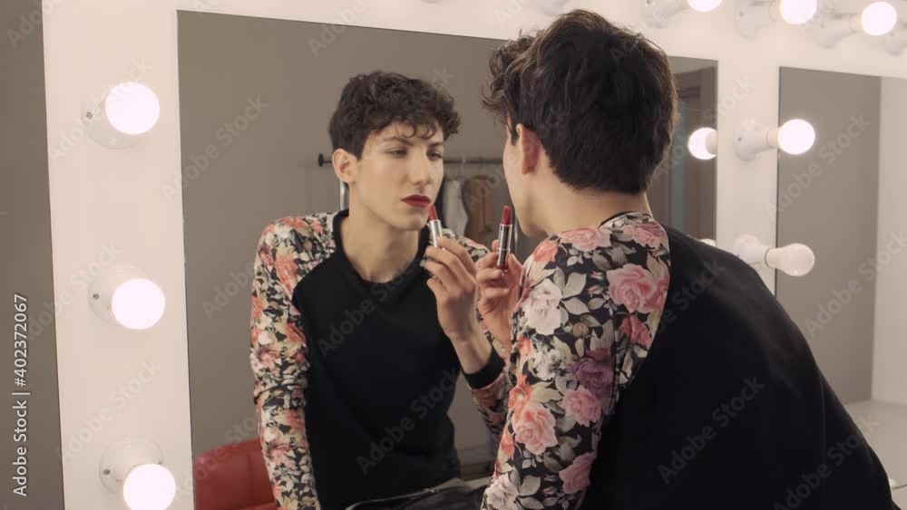 Androgynous man holding lipstick in his hands and paints lips. Young ...