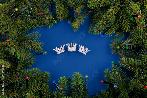 Canvas Print Three crowns on blue background with green branches of spruces and shining garland