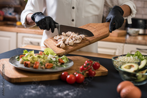Close up of chef hands with kitchen knife cutting meat on a wooden board