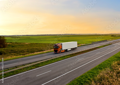 Truck with semi-trailer driving along highway on the sunset background. Goods delivery by roads. Services and Transport logistics.  Modern Lorry Transport concept. Long Self-driving lorries © MaxSafaniuk