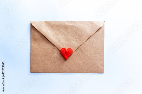 love letter in a craft envelope with clay red heart on light blue background. © EGHStock