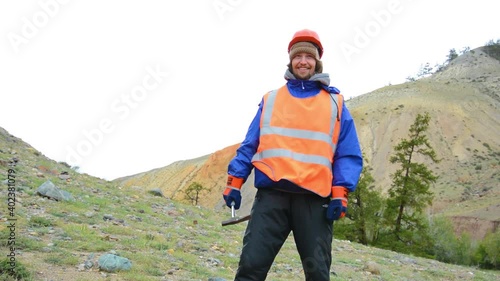Portrait of a mining engineer, a geologist in the protective reflective vest, gloves and helmet, with hammer in hand.