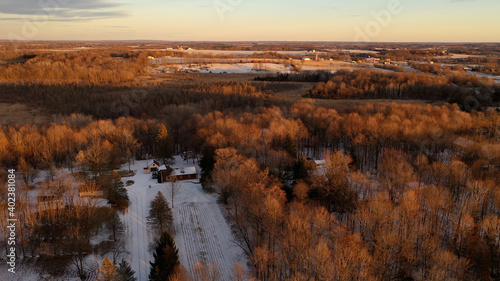  Aerial view of American Midwestern countryside landscape in spring winter season. Agricultural fields covered in snow, farm houses. Sunny, sunset 