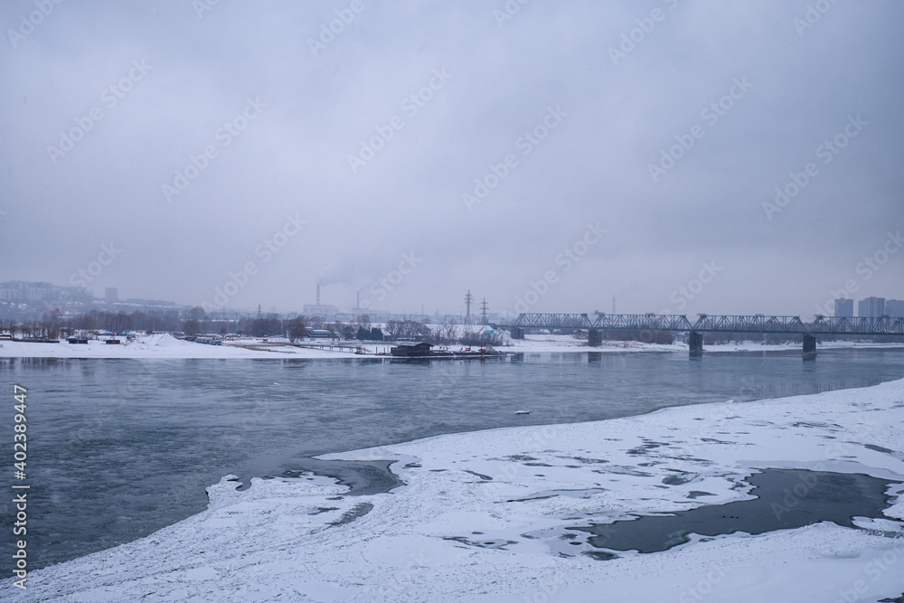 Photo  of the frozen Ob River and railway bridge on a winter snowy day. Novosibirsk, Russia.