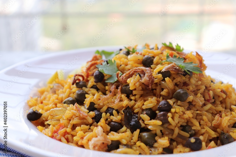 Indian cuisine - Chickpeas Biryani, chole Pulao. Garnished with fried onion, chopped coriander, and lemon wedges. Kala chana biryani. Along with copy space.  