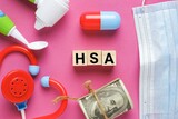 Wooden block written HSA or Healthcare Spending Account with medical toy and covid-19 face mask. One of a number of tax-advantage financial accounts, resulting in payroll tax savings. 