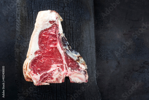 Raw dry aged wagyu t-bone beef steak offered as top view on a rustic charred wooden board with copy space right