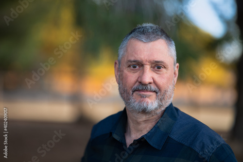 Portrait of an elderly man with a beard and gray hair. A close up with a very soft background in the evening at sunset in warm light. The senior looks friendly.