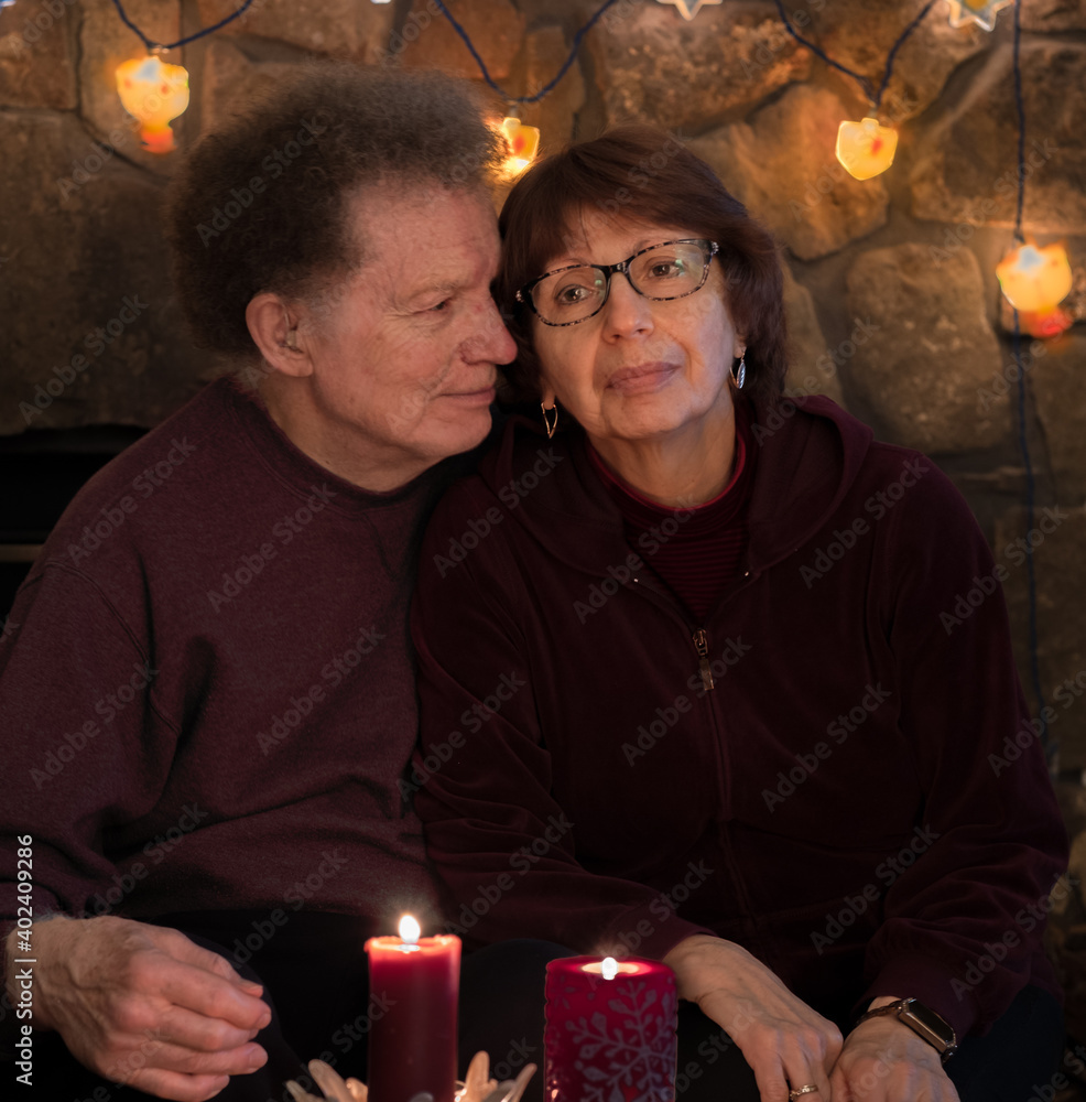 Senior couple sitting in room lit by candlelight; man looking affectionally at sad woman Senior couple sitting in room lit by candlelight; man looking affectionally at sad woman