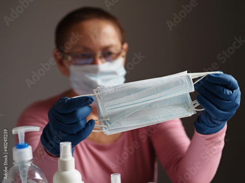 Protective gear to prevent viral infection such as hand sanitizer, surgical medical masks and rubber protective gloves.Elderly woman on gray background holding masks. photo