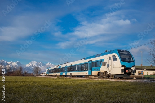 Modern diesel passenger train in white and blue color approaching small station of Rodica on a sunny winter day.
