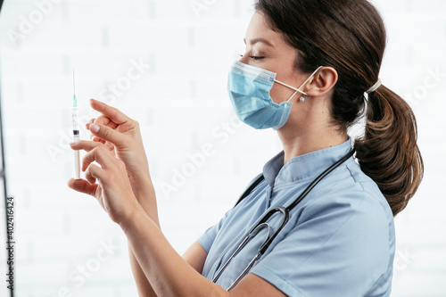 Beautiful female doctor with medical mask. Portrait of nurse with syringe in her hand..