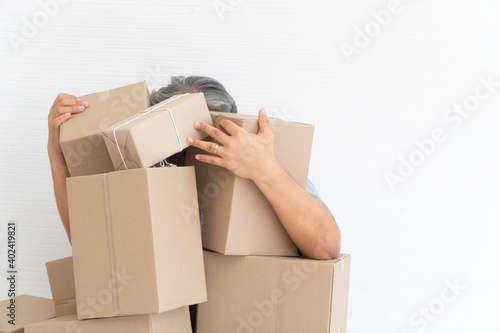 Asian Shopaholic sitting on the floor in the living room and Cardboard Box on top of him after The courier delivered to the home. Concept of shopping online and Shopaholic. © Prot