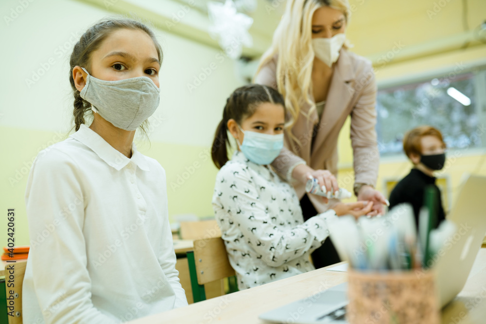 Pupils sit at their desks in medical masks and the teacher disinfects their hands. Virus protection Pupils sit at their desks in medical masks and the teacher disinfects their hands. Virus protection