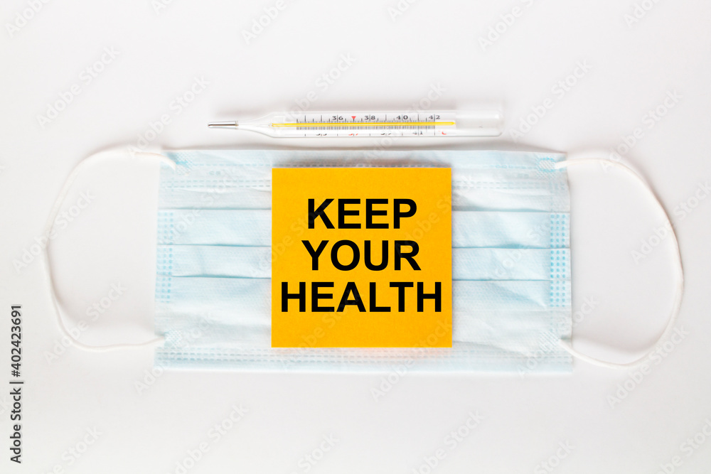 Sticker with text Keep Your Health lying on the mask with a thermometer. Sticker with text Keep Your Health lying on the mask with a thermometer.