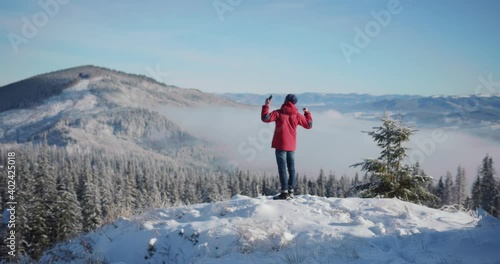 Excited young man hiking in mountains using smartphone celebrating winter holidays on moutain top. Picturesque scenery. White landscape. photo