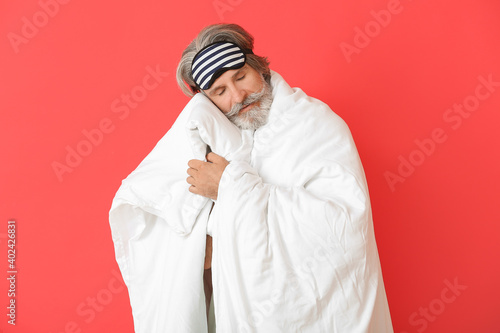 Mature man in sleep mask on color background