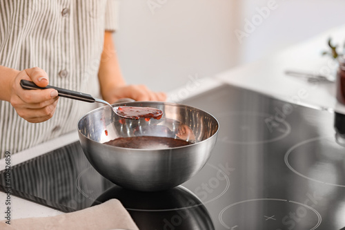 Woman cooking sweet raspberry jam in kitchen