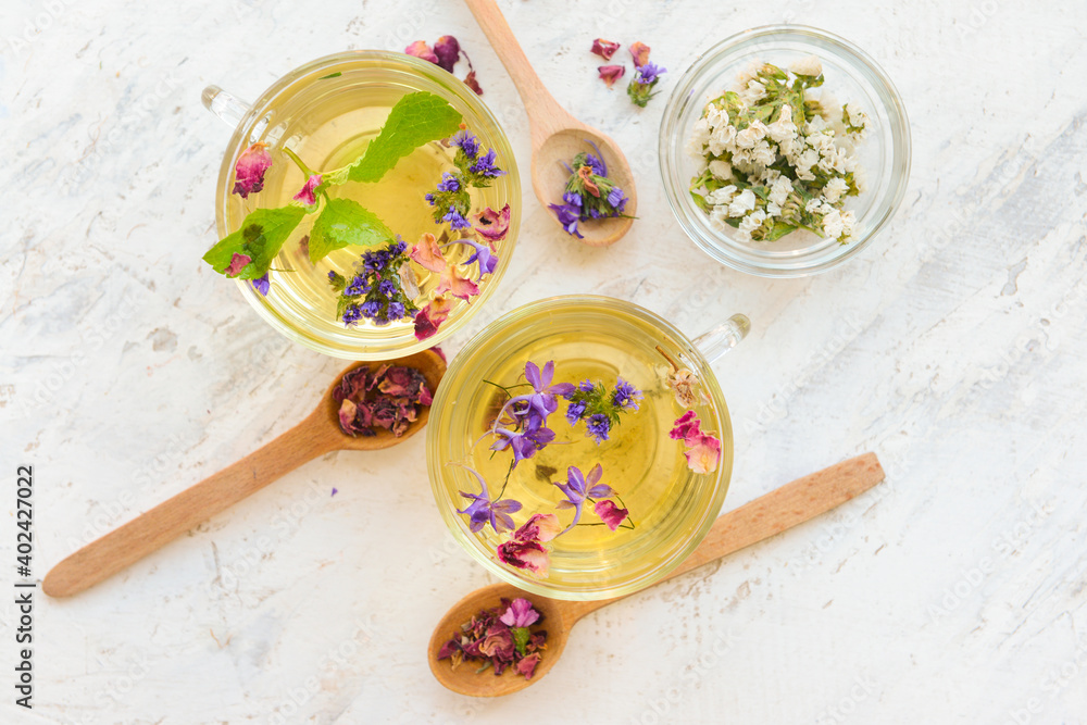 Fototapeta premium Cups with floral tea and herbs in spoons on light background