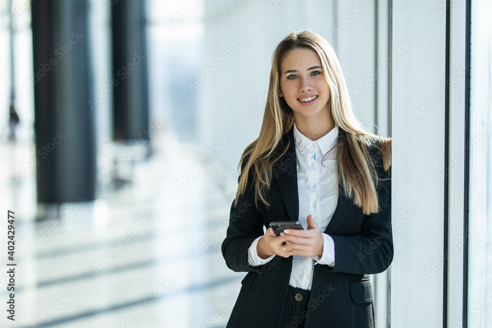Smiling business woman standing in office with mobile phone in hand looking at camera. Smiling business woman standing in office with mobile phone in hand looking at camera.