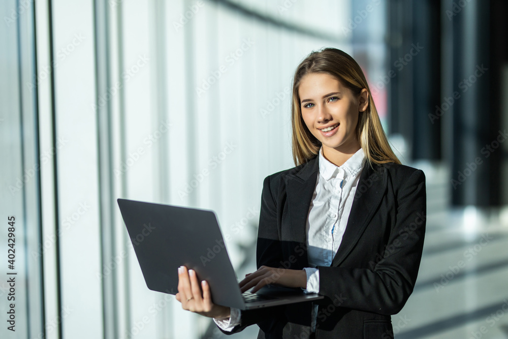 Young business woman with laptop standing in an office with panoramic windows Young business woman with laptop standing in an office with panoramic windows