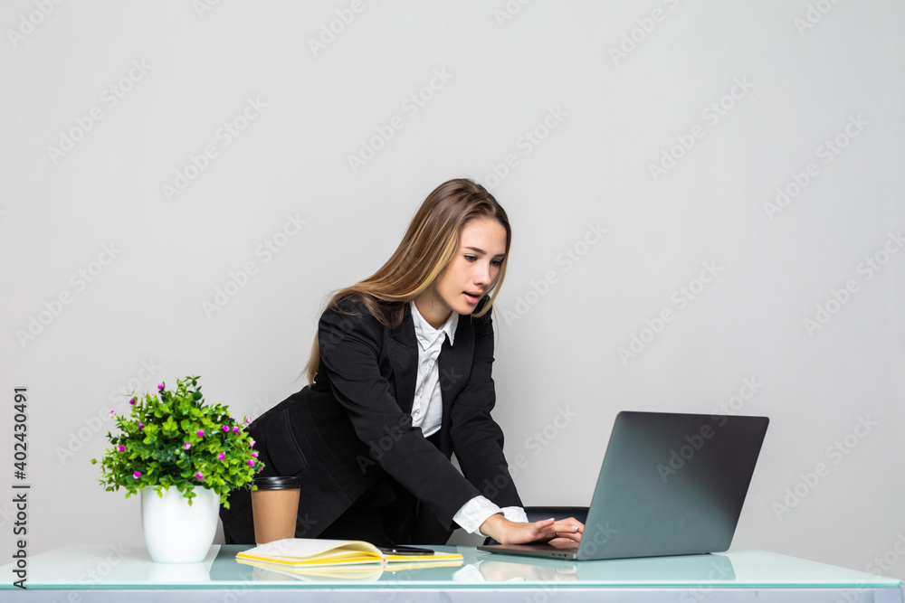 Young businesswoman leaning over her desk and working on a laptop in a large modern office Young businesswoman leaning over her desk and working on a laptop in a large modern office