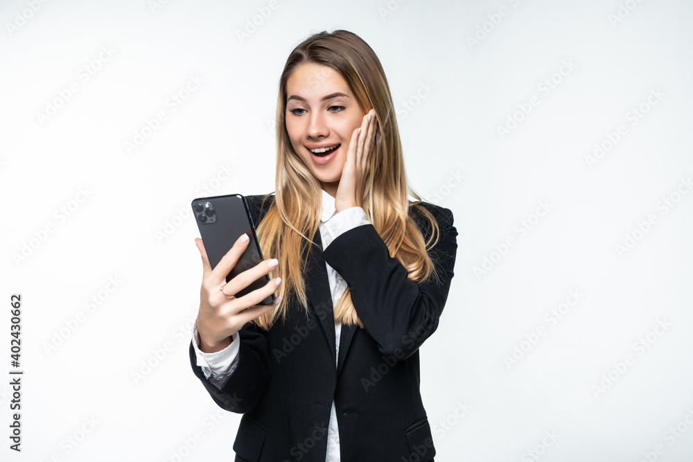 Portrait of surprised and impressed business woman with widened eyes and opened mouth, stunned on phone while standing against white background. Girl uses some app Portrait of surprised and impressed business woman with widened eyes and opened mouth, stunned on phone while standing against white background. Girl uses some app