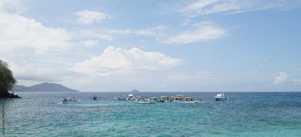 Boats and people visiting Tropical Blue Lagoon Beach near Bali in Indonesia.