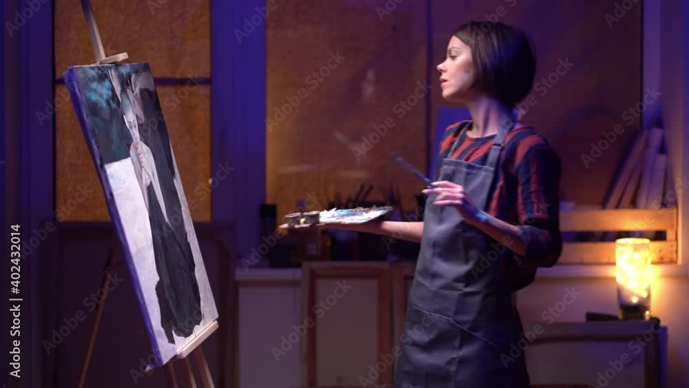 .Female artist Working on oil painting. In her hands are brushes and a palette. She paints a picture in the mysterious atmosphere of her studio. .Female artist Working on oil painting. In her hands are brushes and a palette. She paints a picture in the mysterious atmosphere of her studio.
