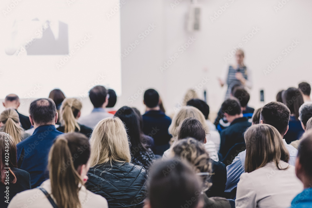 Obraz premium Business and entrepreneurship symposium. Female speaker giving a talk at business meeting. Audience in conference hall. Rear view of unrecognized participant in audience. Copy space on whitescreen.